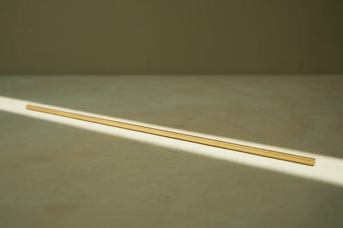 A fine brass rod laid perfectly parallel to a narrow band of light, illuminated along its entire length