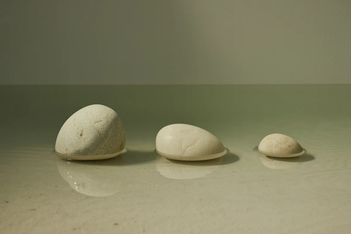 Three pale stones of different sizes in a row at different apparent depths in shallow clear water