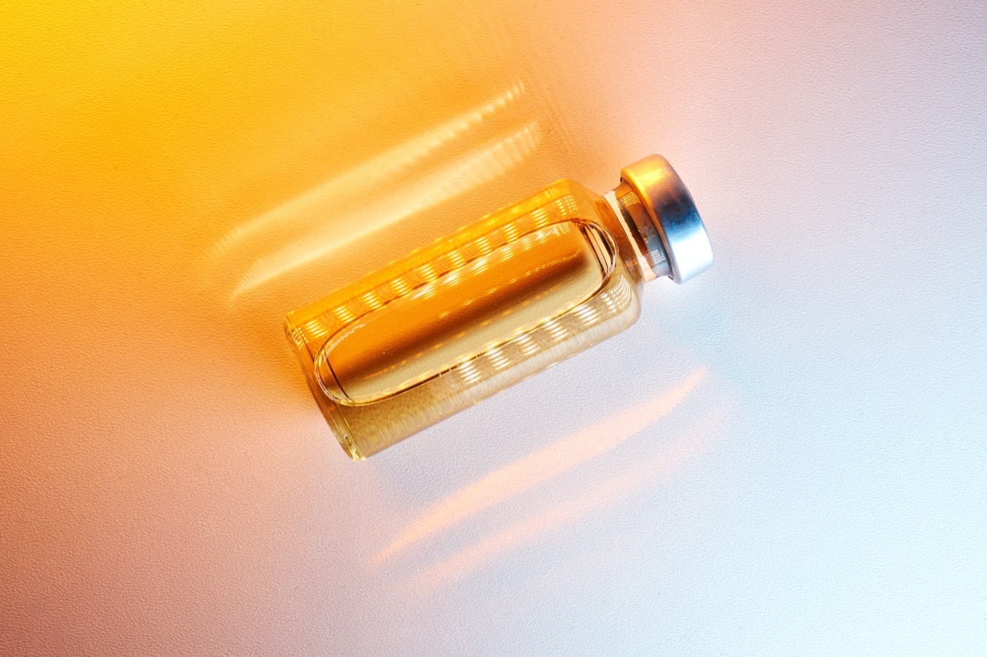 An unlabeled amber glass vial with a silver crimp cap on a warm gradient surface